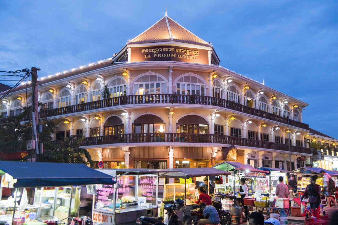 Evening shot of the Ta Prohm Hotel in Cambodia, its grand architecture illuminated above a vibrant street market bustling with locals and tourists